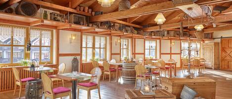 Un interior rústico de madera con múltiples mesas y sillas de comedor, un barril de madera grande y un candelabro rústico.