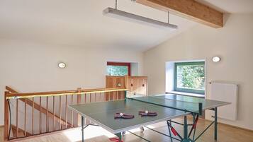 A spacious room with a ping pong table, a wooden staircase, and a window with a view of greenery.