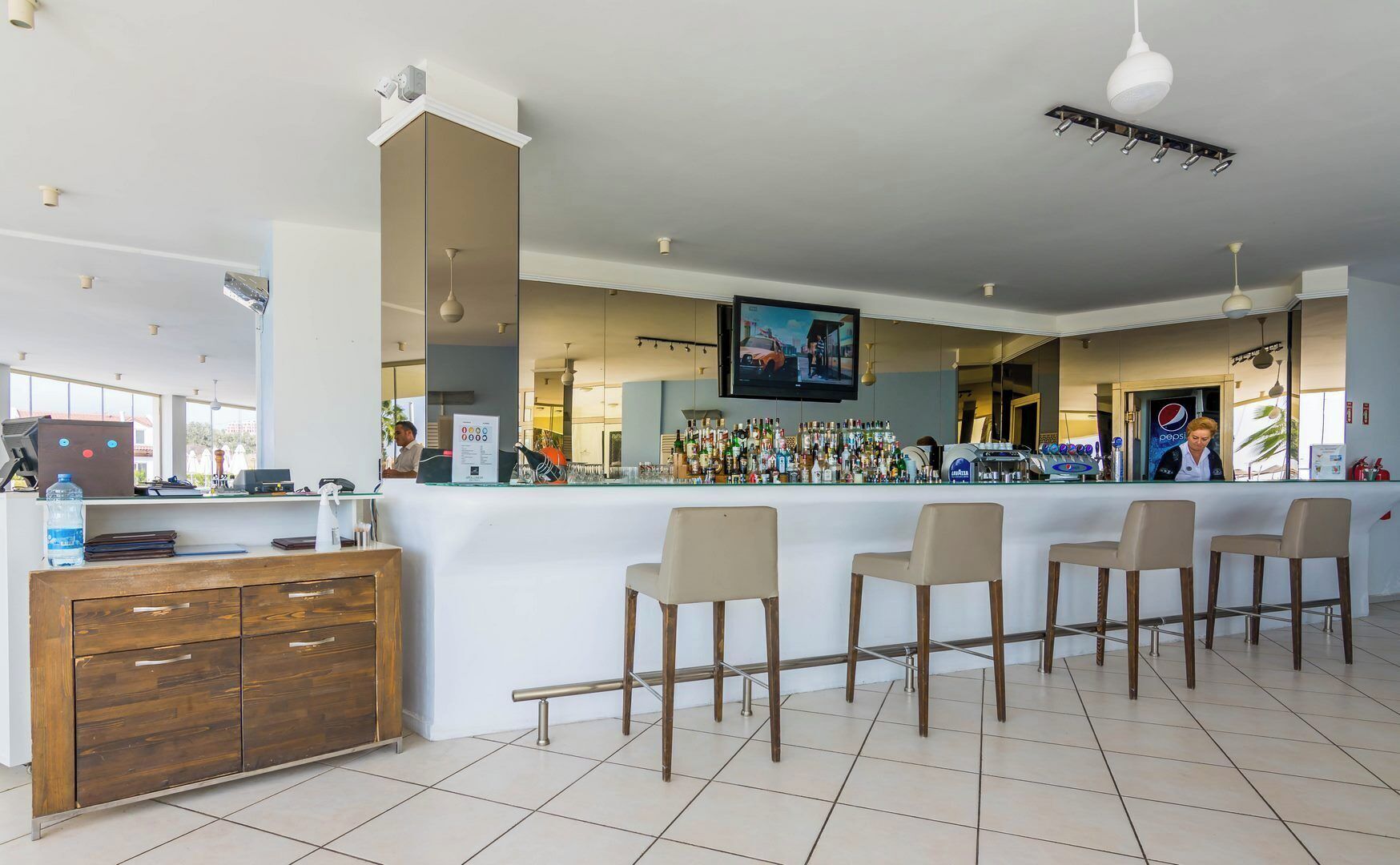 Una zona de bar con mostrador, taburetes, una pantalla de televisión y una variedad de botellas.