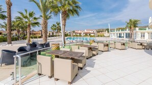 A rooftop pool area with lounge chairs and tables, surrounded by palm trees and a clear blue sky. - Apollonium Bozbuk (Milas)