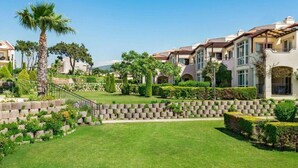 A residential area with multi-story houses, a well-maintained lawn, and a stone wall. - Apollonium Bozbuk (Milas)
