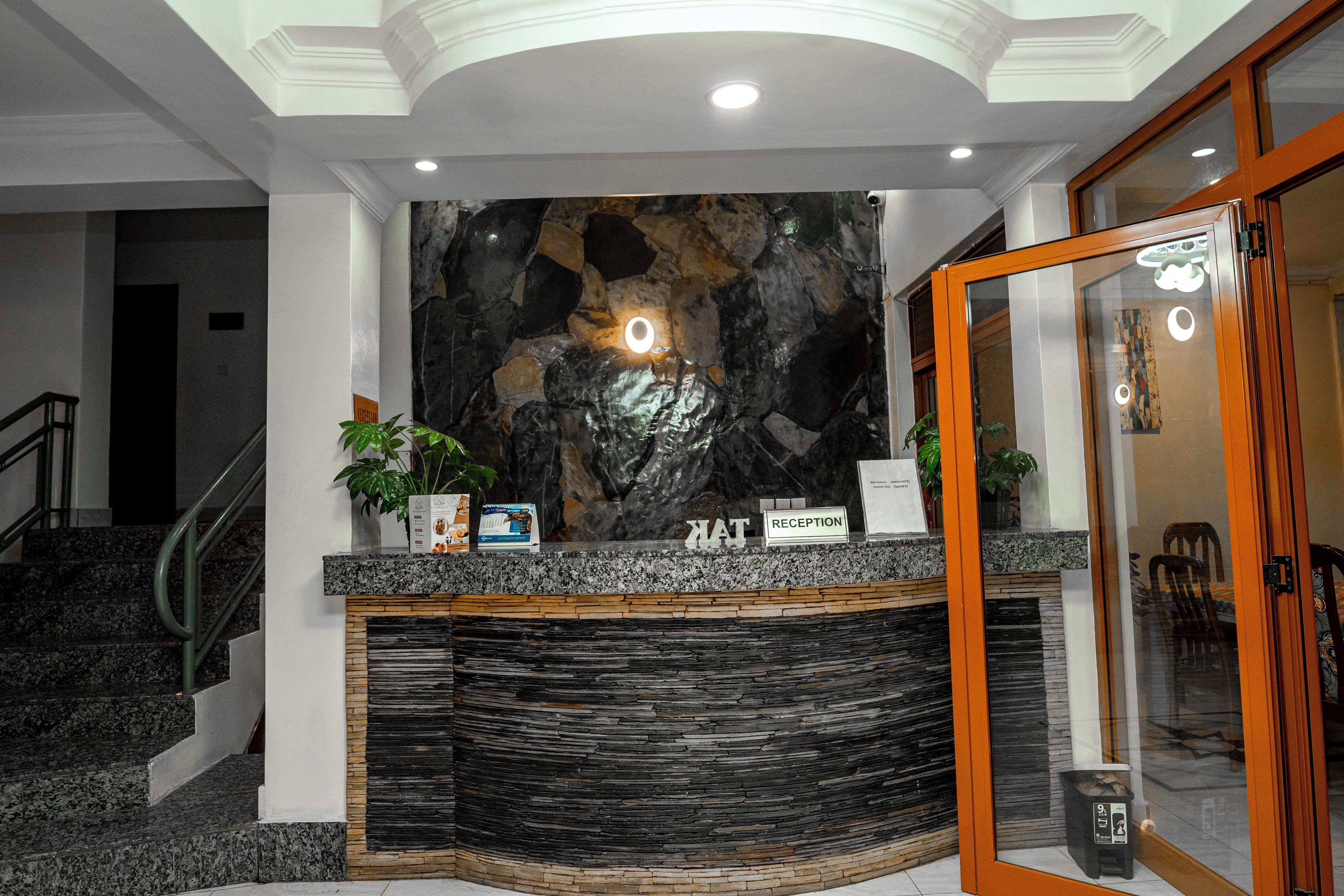 A reception desk with a stone wall backdrop, a staircase to the left, and a glass door to the right.