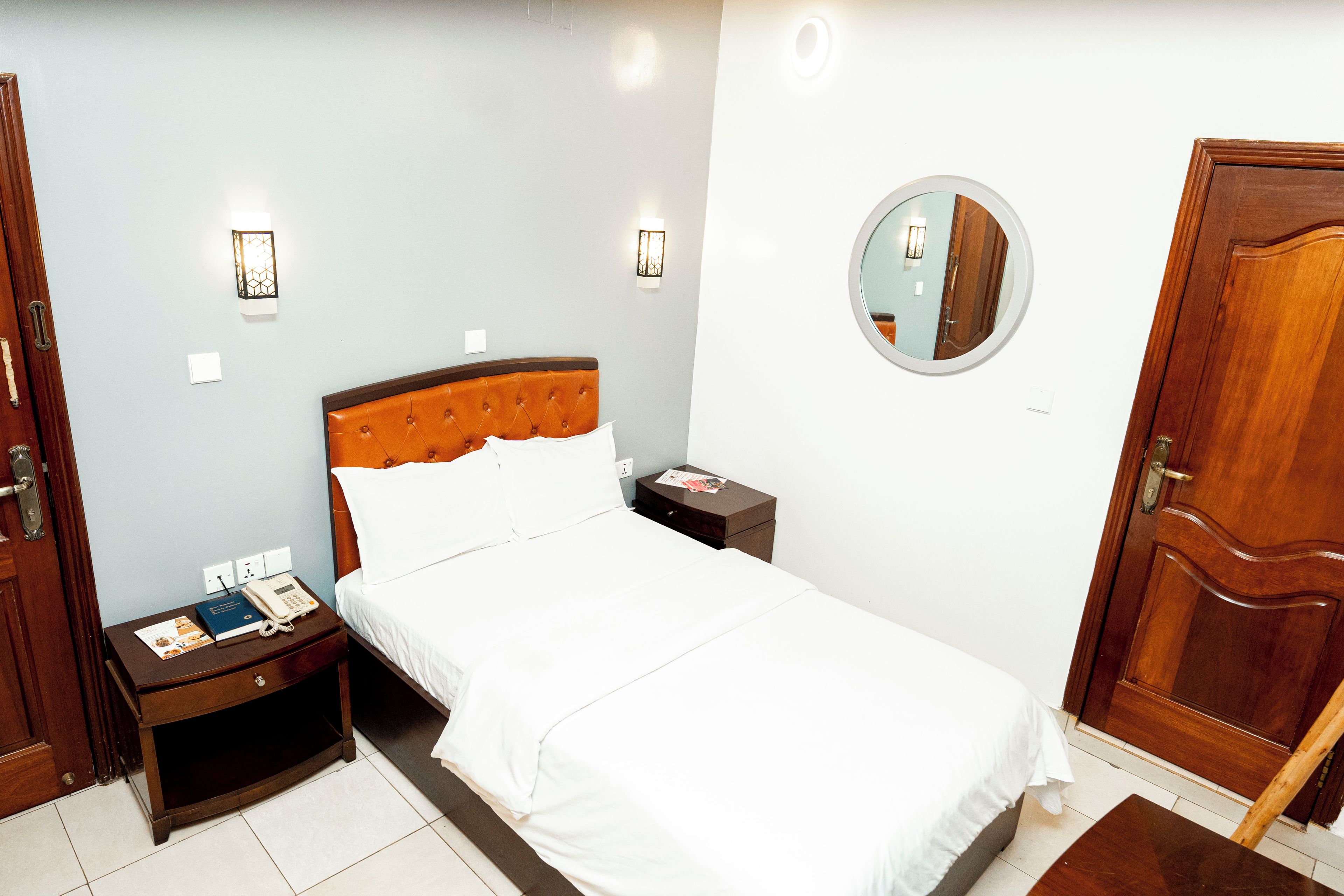 A hotel room with a bed, bedside tables, a mirror, and a door.