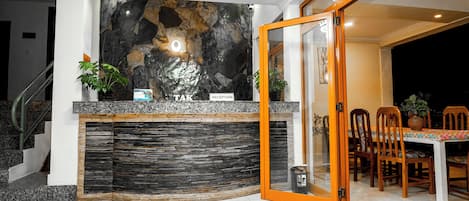 A reception area with a stone wall, a reception desk, and a dining area with chairs and a table.