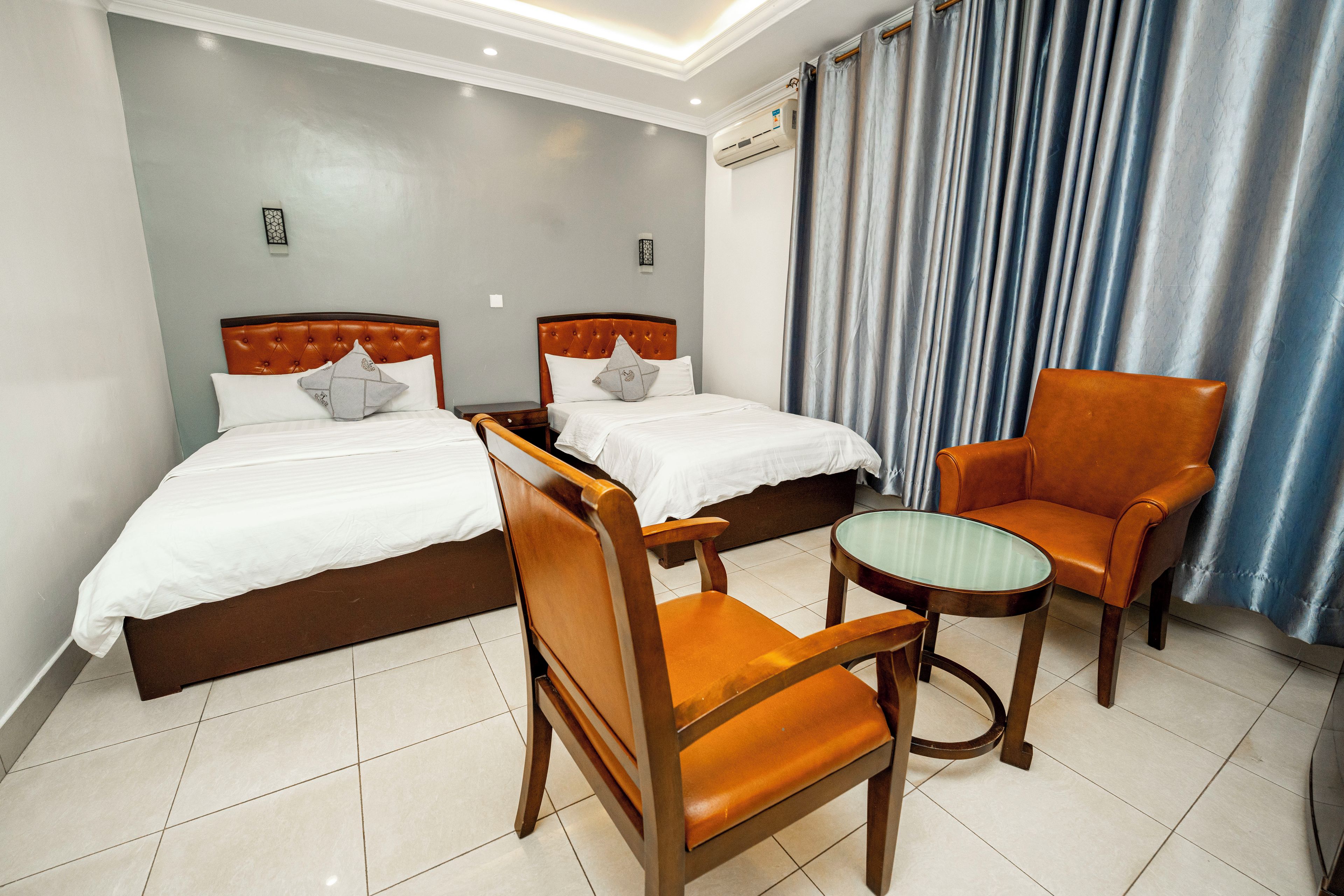 A hotel room with two beds, a chair, a small table, and a curtain.