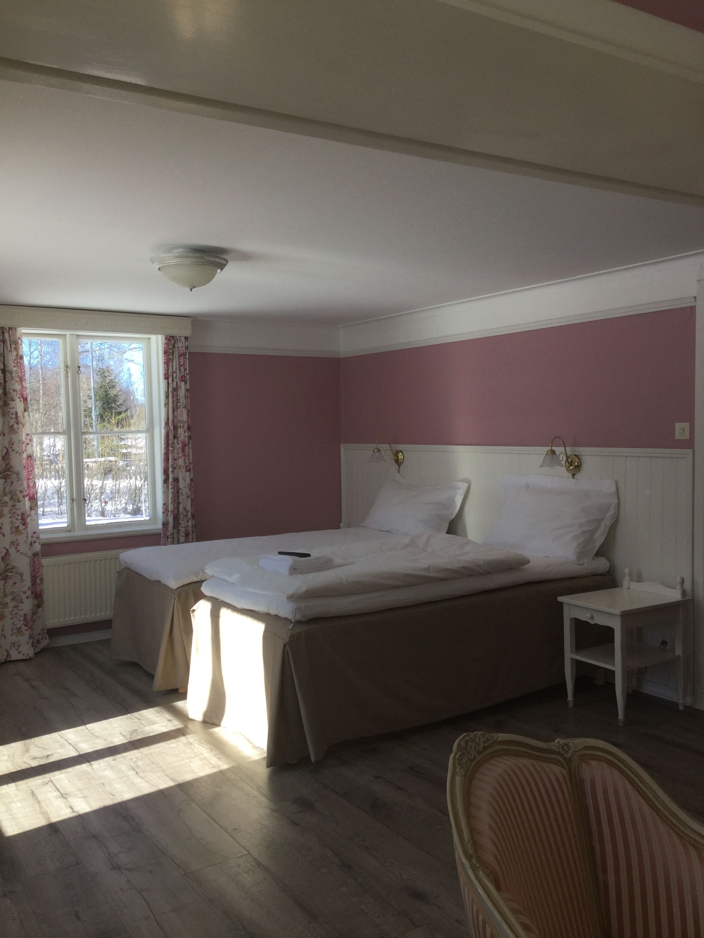 A bedroom with a bed, a nightstand, a chair, and a window with curtains.