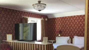 A hotel room with a striped partition, a bed, a desk with a computer, a red armchair, and a chandelier.
