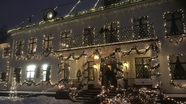A building with multiple windows and balconies, decorated with lights and garlands, surrounded by snow. - Hellefors Herrgård (Hallefors)