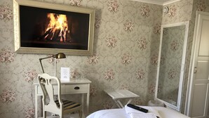 A hotel room with a bed, a desk with a chair, a television displaying a fireplace, and a door. - Hellefors Herrgård (Hallefors)