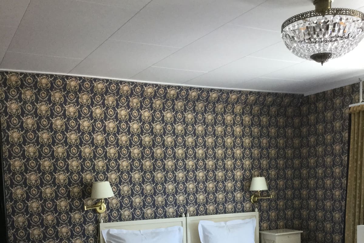 A bedroom with a bed, two bedside tables, a chair, a desk, and a chandelier.