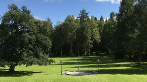 A well-maintained lawn with a circular water feature and street lamps, surrounded by trees. - Hellefors Herrgård (Hallefors)