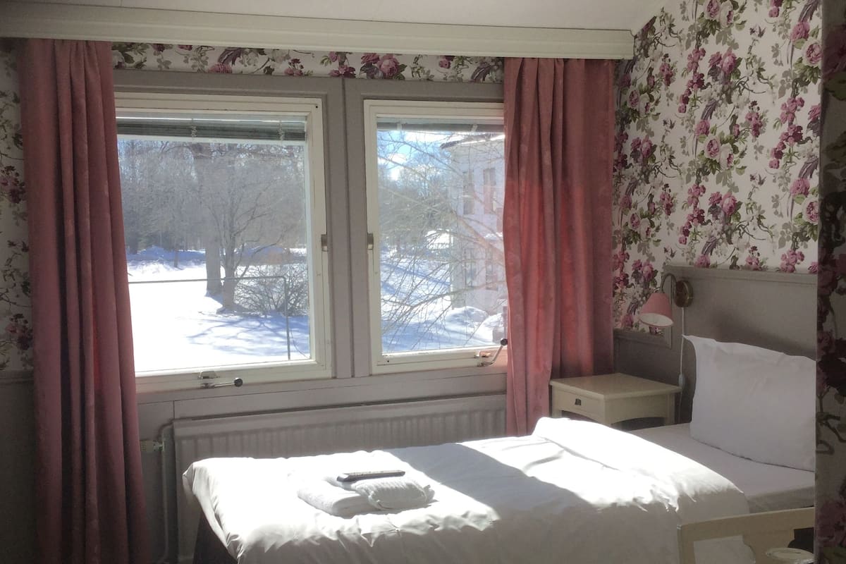A bedroom with a bed, a bedside table, a lamp, and a view of a snowy landscape through the window.