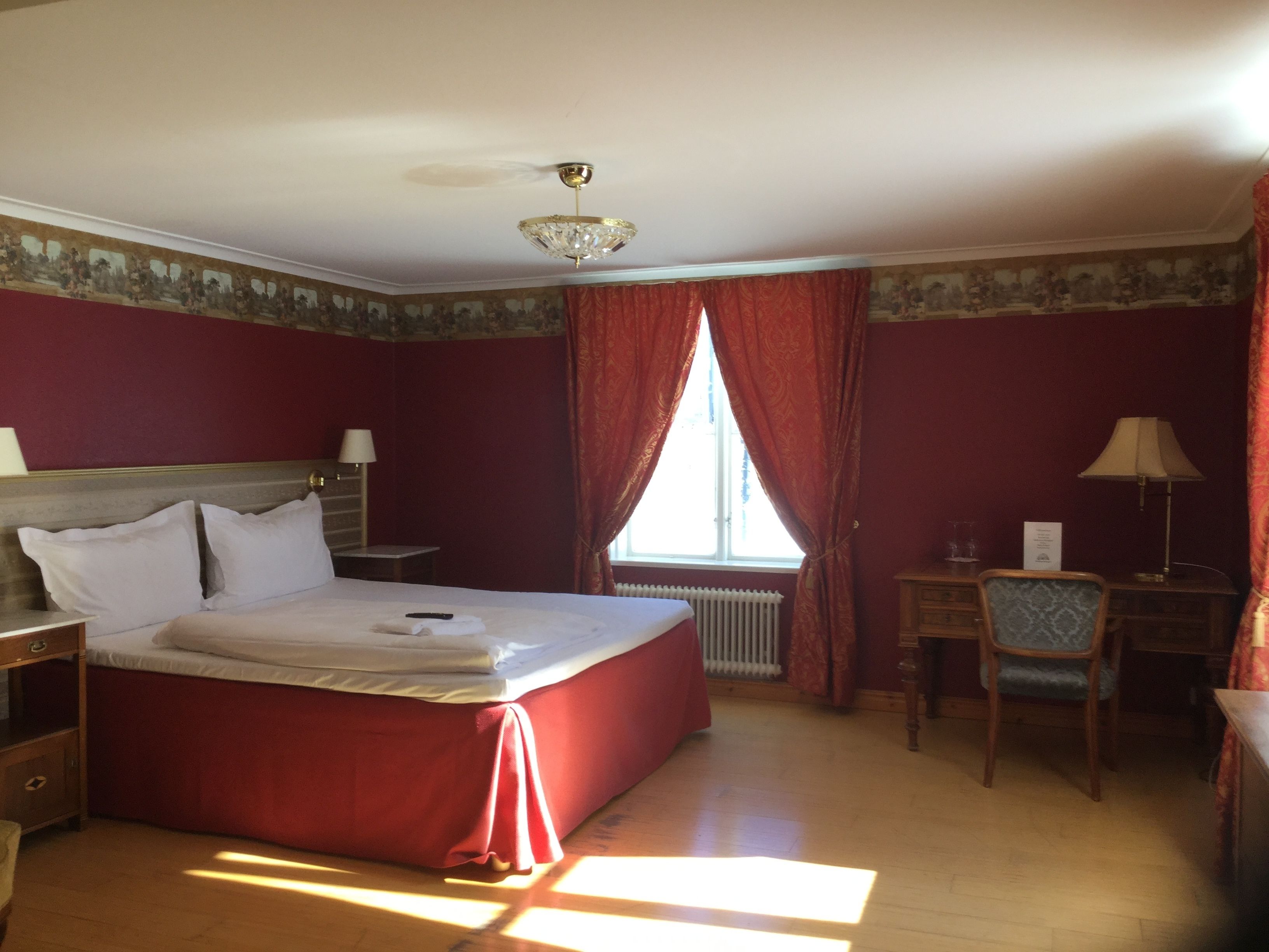 Hotellihuone, jossa on suuri sänky, työpöytä, tuoli ja ikkuna, jossa on verhot.