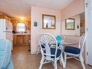 Una cocina compacta con armarios de madera, un refrigerador blanco y un comedor con una mesa de vidrio y sillas de mimbre blanco.