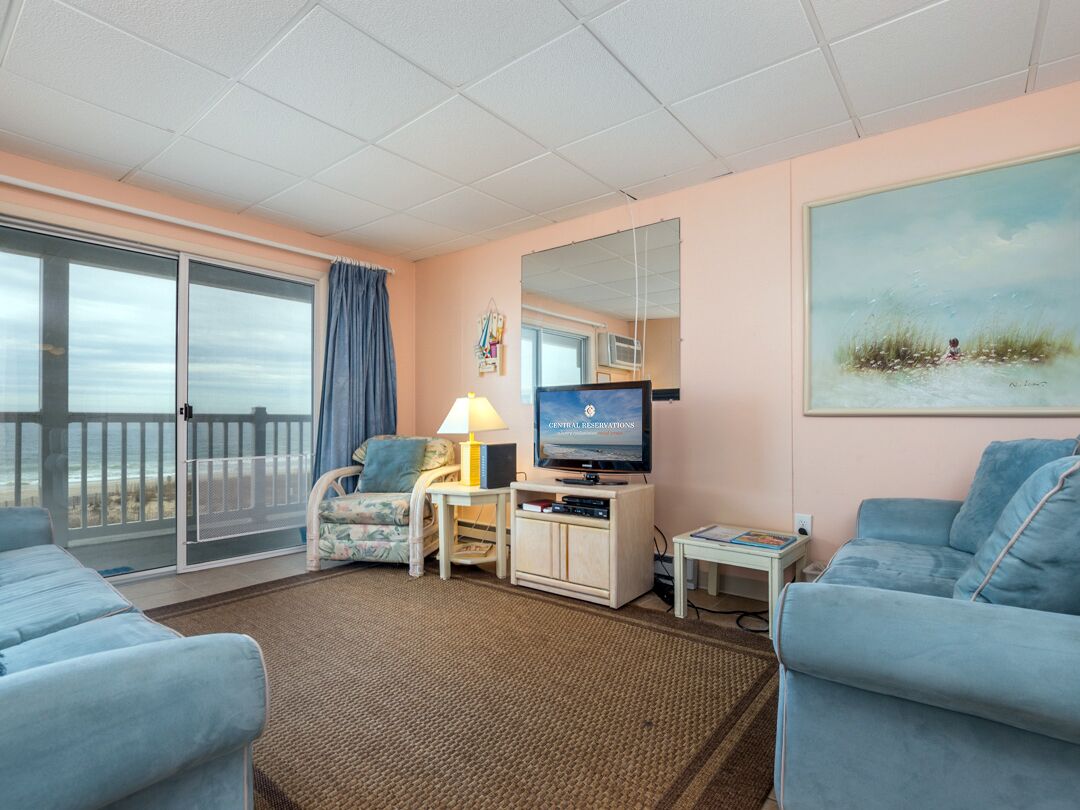 Et værelse med fjernsyn, sofa, stol, skrivebord med lampe og et maleri på væggen.
