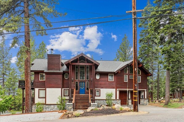 A two-story wooden cabin with a stone foundation, a blue front door, and a staircase leading to the entrance. - Dollar Point Retreat: High-Ceiling Lakeview Villa Perfect for Large Groups (Tahoe City)