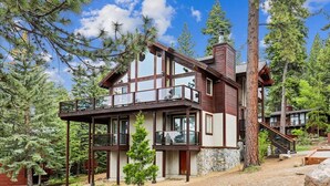 A multi-story wooden cabin with a balcony, surrounded by pine trees.