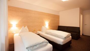 A hotel room with two beds, a dark sofa, and wooden paneling on the walls.