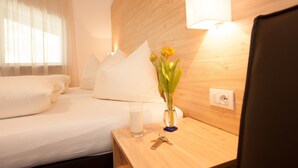 Habitación de hotel con una cama, una mesita de noche con un florero, un vaso de agua y una lámpara.