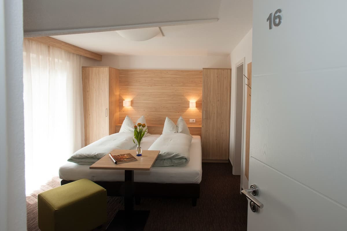 Habitación de hotel con cama, lámparas de noche, una mesita con un florero y una silla verde.