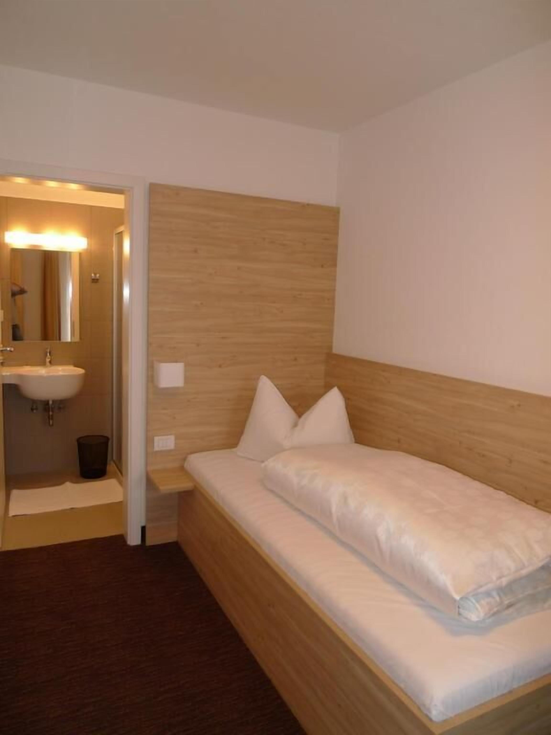 A single bed with a wooden headboard, a bedside table, and a mirror.