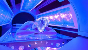 Una persona recostada sobre una cama curva y transparente, con estructura metálica, iluminada con luces azules.