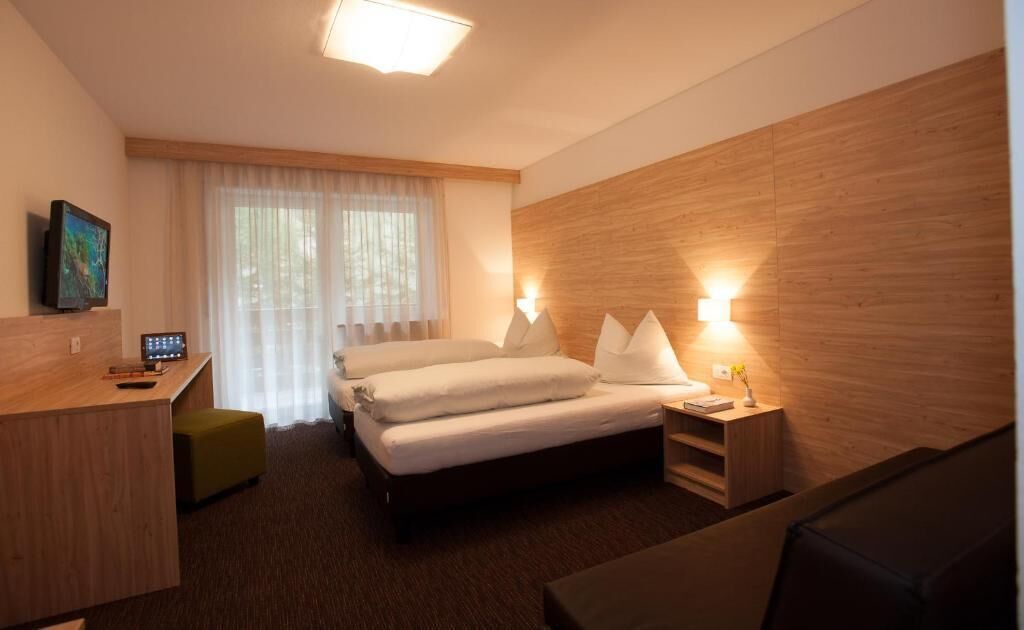A hotel room with a bed, bedside tables, a desk, a chair, and a window with curtains.