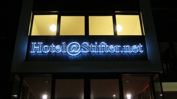 Un letrero de hotel con el nombre "Hotel@Stifter.net" iluminado con luces de neón azules.