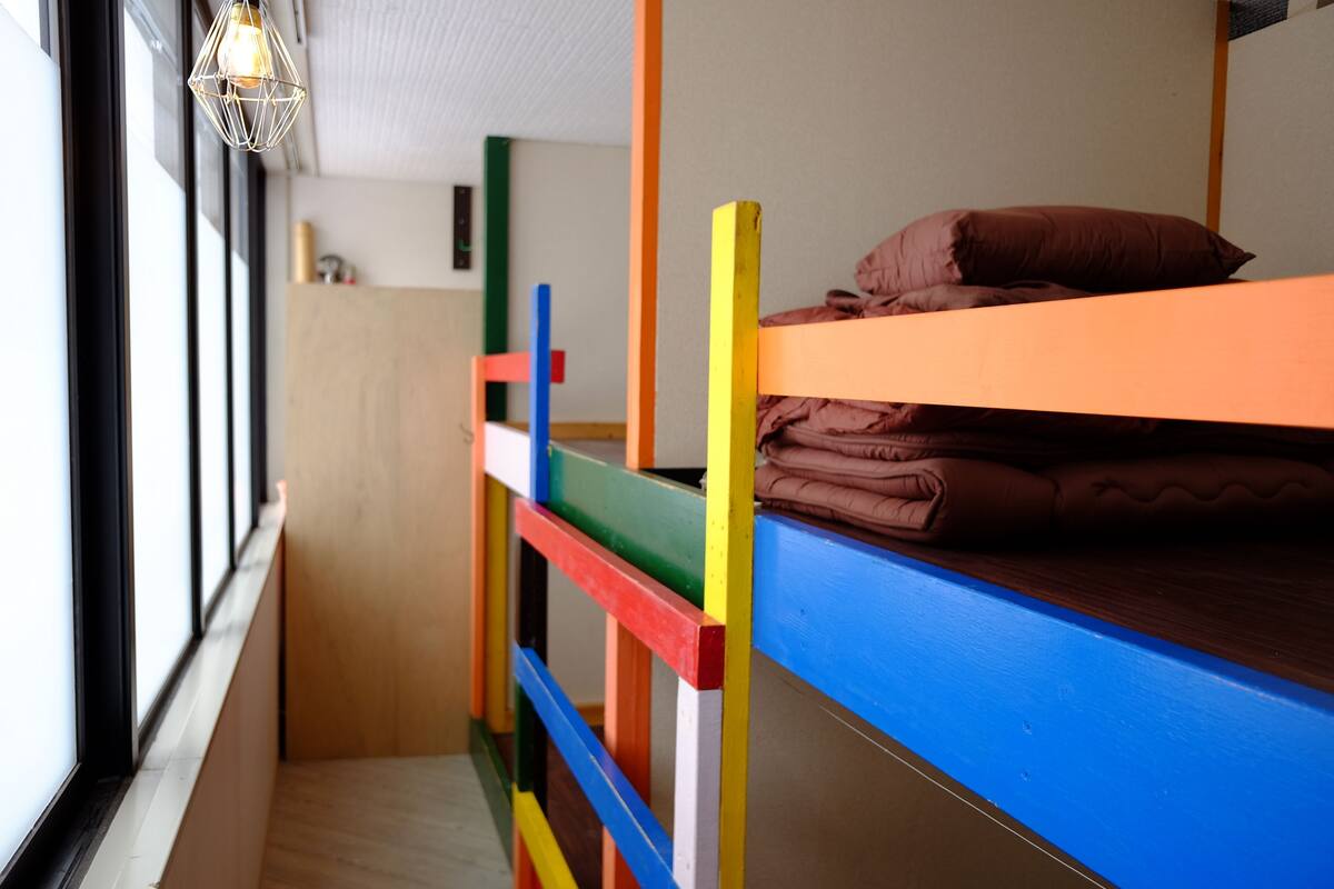 A bunk bed with colorful railings in a room with a window and a hanging light fixture.