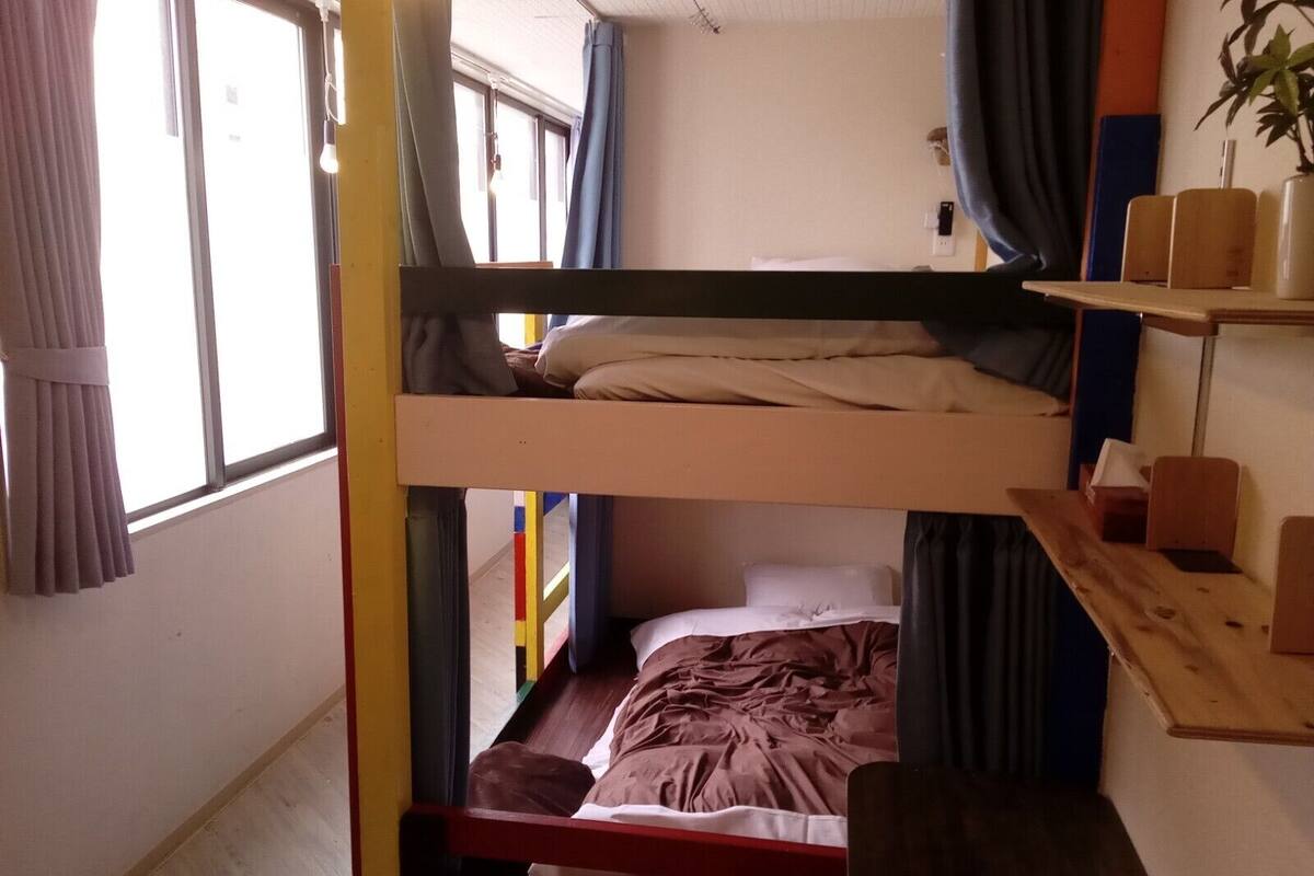 A bunk bed room with a window, curtains, and a shelf with items.