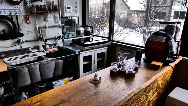 A kitchen with a wooden countertop, a sink, and various kitchen appliances. There is a window with a view of a snowy landscape. - Guest House Asahikawa Ride - Hostel (Asahikawa)