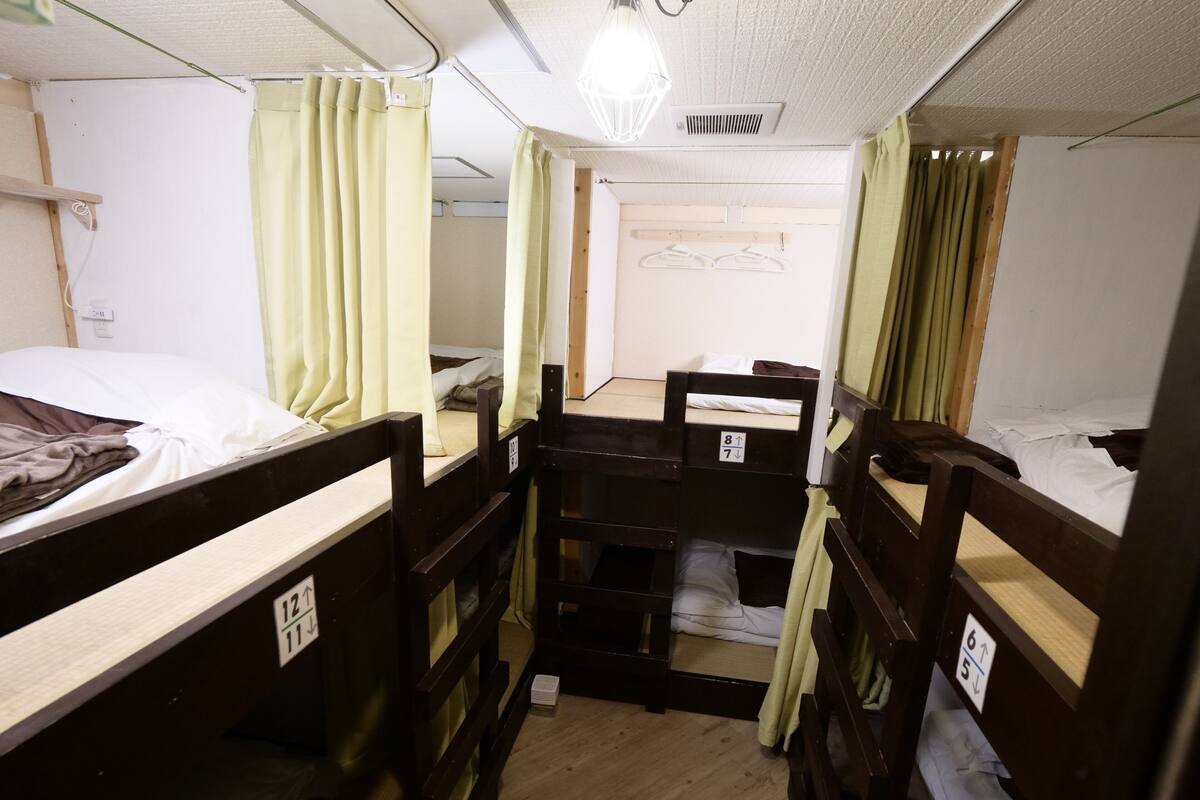 A dormitory room with bunk beds, a small desk, and a hanging light fixture.