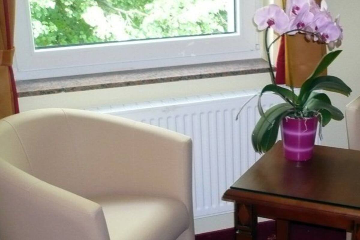 A room with two beige armchairs, a small wooden table, and a window with a view of greenery.