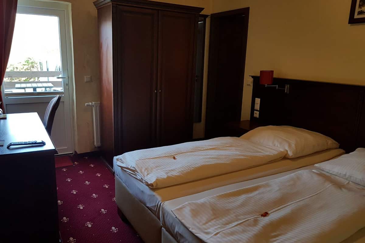 A hotel room with two beds, a desk, a wardrobe, and a window.