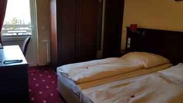 A hotel room with two beds, a desk, a wardrobe, and a window.