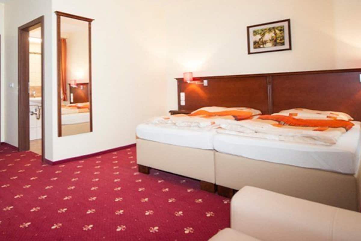 A hotel room with a bed, a desk, and a chair. There is a mirror on the wall and a picture above the bed.