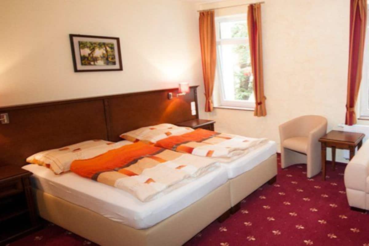 A hotel room with a bed, a sofa, a small table, a TV, and windows with curtains.