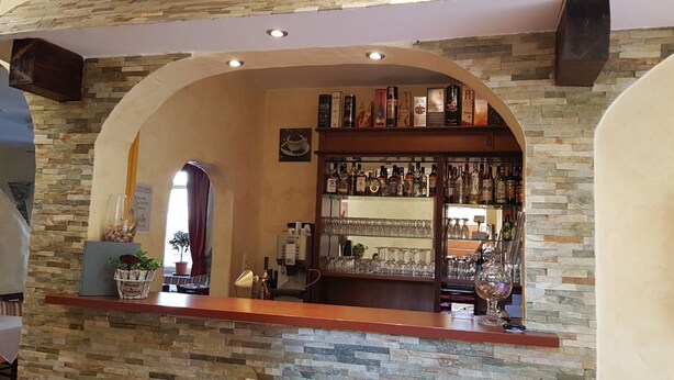Zona de bar con pared de piedra, estantes con botellas de licores y una máquina de café.
