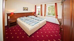 Una habitación de hotel con una cama doble, dos mesitas de noche, una ventana con cortinas y un cuadro pequeño en la pared.