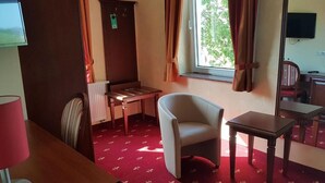 Habitación de hotel con cama, escritorio, silla, televisión, ventana con cortinas y radiador.