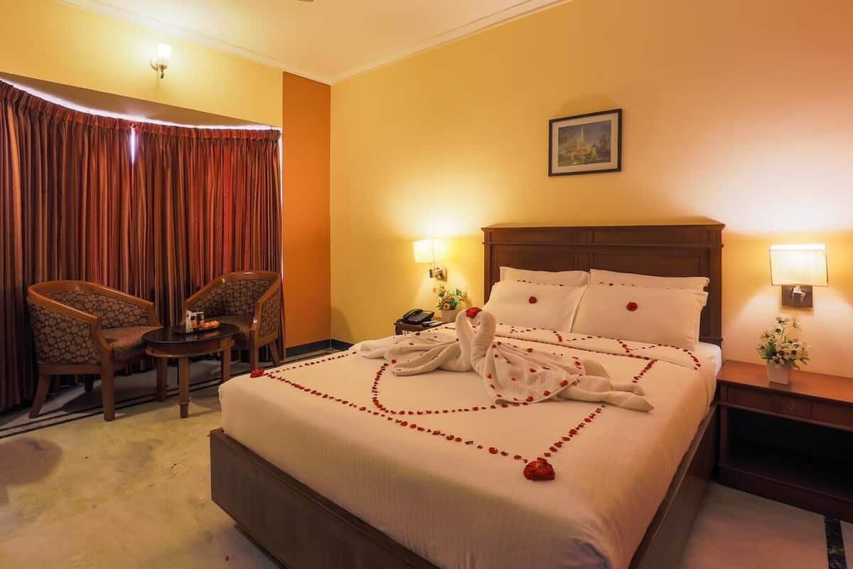 A hotel room with a large bed, two bedside tables, a nightstand, a chair, and a curtain.