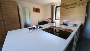 A modern kitchen with a white countertop, a built-in stove, a sink, and a wooden door. - Camping les Vernières (La Bourboule)