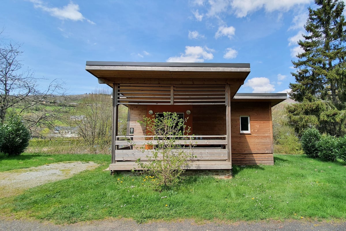 Una cabaña de madera con un porche, rodeada de follaje y árboles.