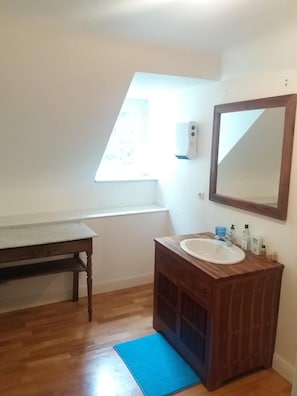 A bathroom with a wooden vanity, a white sink, a mirror, and a blue mat on the floor.