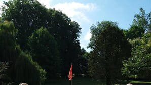 A stone lion statue in a garden with a flagpole and chairs in the background. - Château de Grand Tonne (Thue et Mue)