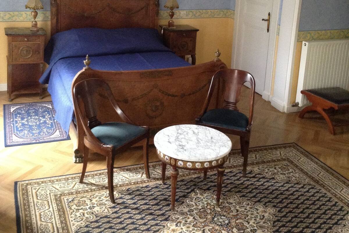 A bedroom with a wooden bed, two nightstands, a chair, a small round table, and a door.