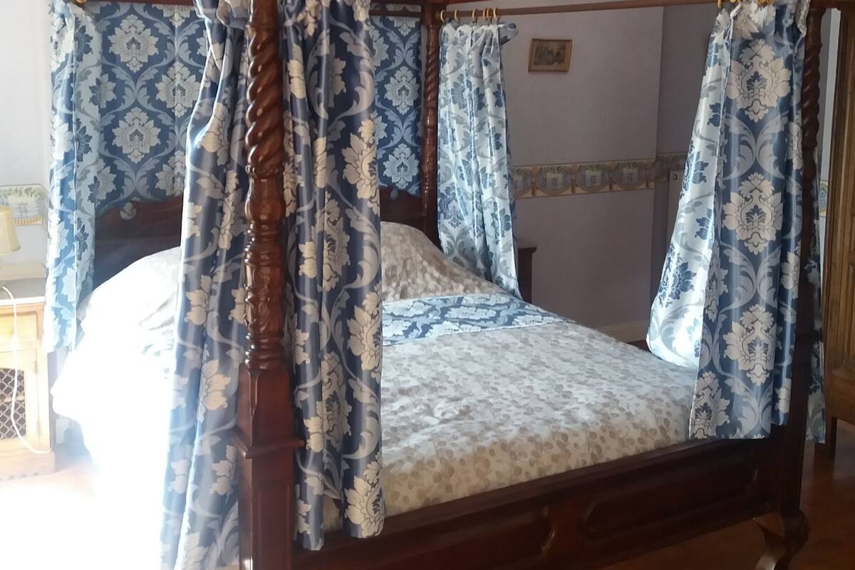 A four-poster bed with floral-patterned curtains, a wooden headboard, and a chandelier.