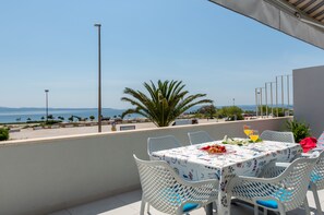 A terrace with a table set for two, overlooking a beach and the sea. - Beachfront Holiday Apartments (Split)