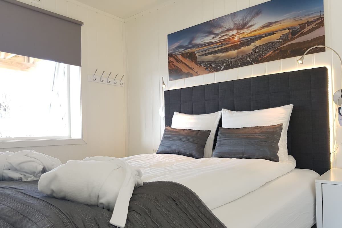 A neatly made bed with a headboard, a bedside lamp, and a wall-mounted clock.
