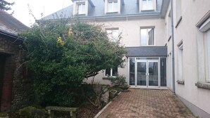 A courtyard with a paved walkway, a stone bench, and a large tree. - Jackotel Orleans (Orléans)